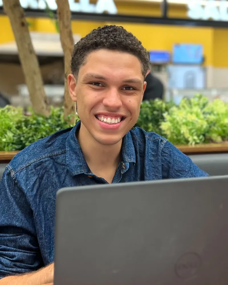 João Gabriel Borela de Abreu, sorrindo, sentado diante de um notebook